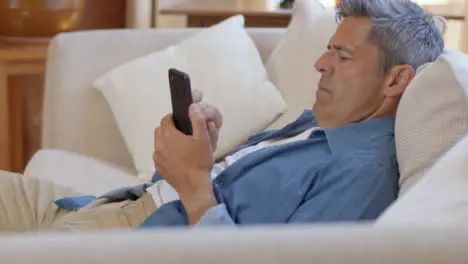 Tilting Shot of Middle Aged Man Slouched On Sofa Using Smartphone 