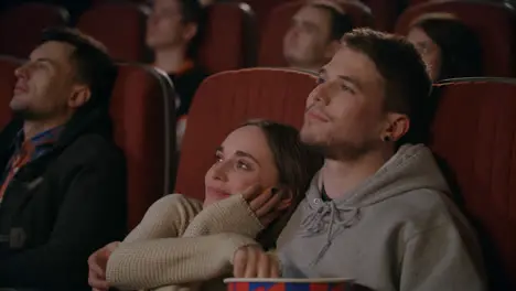 Guy embracing girl while watching movie in cinema Love couple enjoy movie