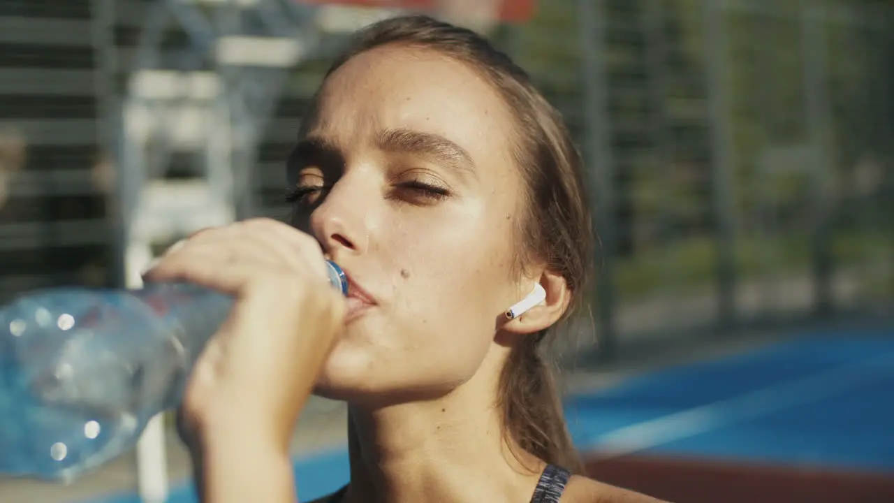 Close Up Of A Sporty Woman Standing At An Outdoor Court Resting And Drinking Cold Water After Workout