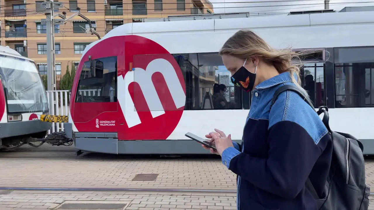 Woman citizen with mobile walking in the street with tram passing by