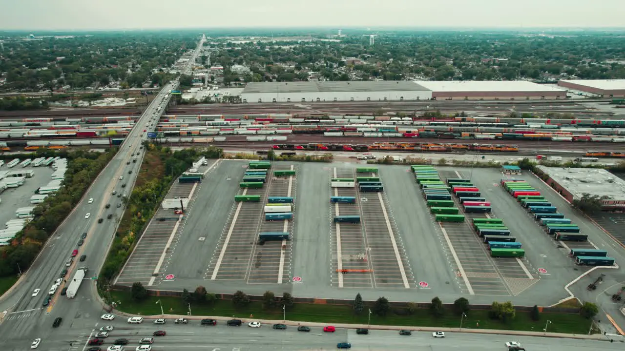 Large Freight Terminal next to a Train Cargo Complex with Wagons and Trailers of Difrent Colors next to a Road full of Traffic