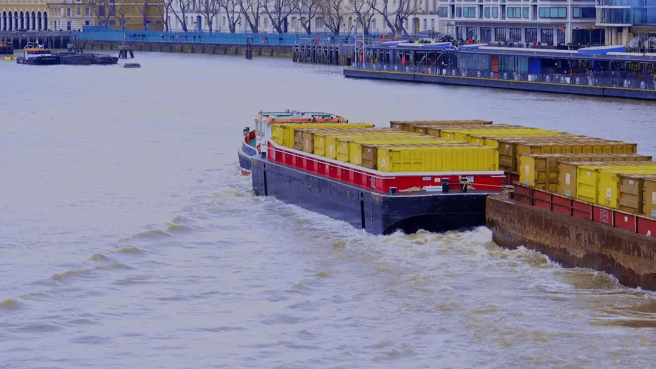 A small tug boat towing three barges full of containers under the Tower bridge and up the Thames River in London