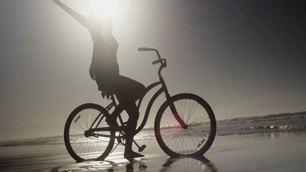 Silhouette of woman sitting with arms outstretched on bicycle