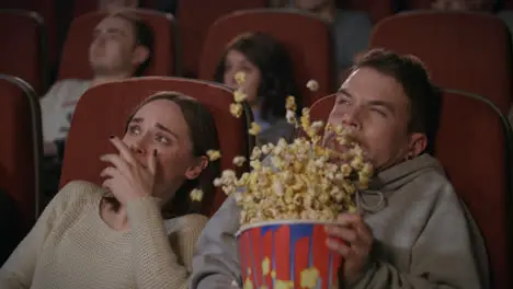 Young couple watching horror film in movie theatre Guy sprinkle popcorn