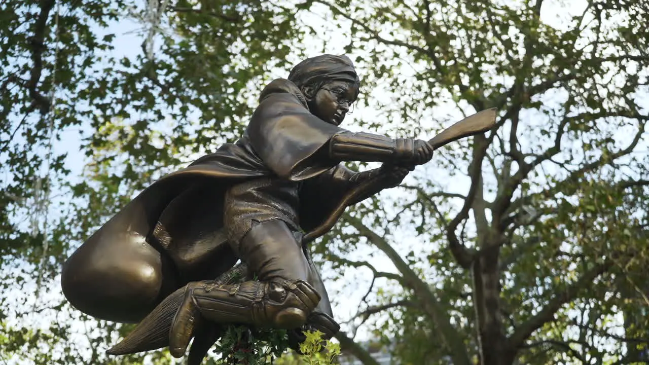 Iconic statue of Harry Potter flying on broomstick at Leicester Square in London with trees blowing in background