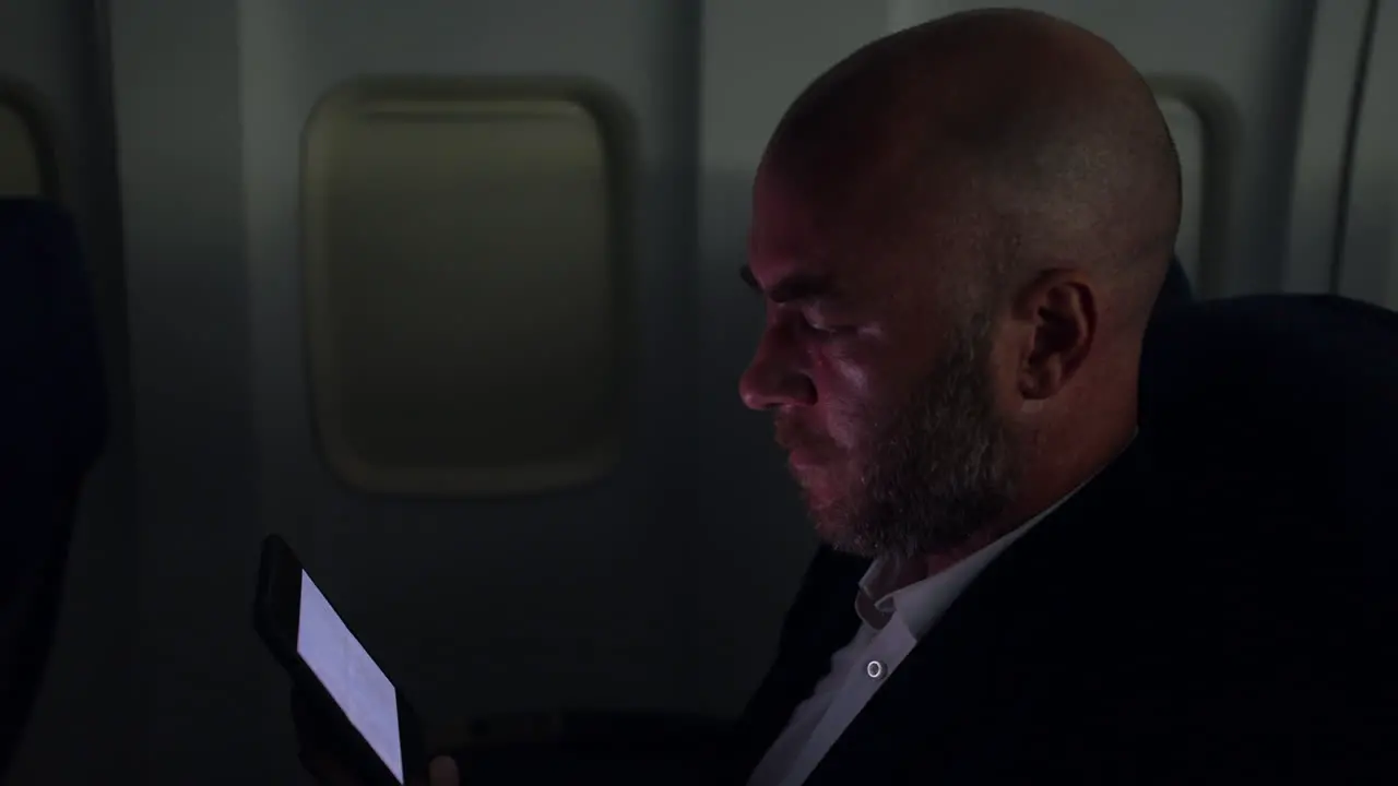 A man watching a video on a tablet on a passenger plane airliner at night in a dark cabin