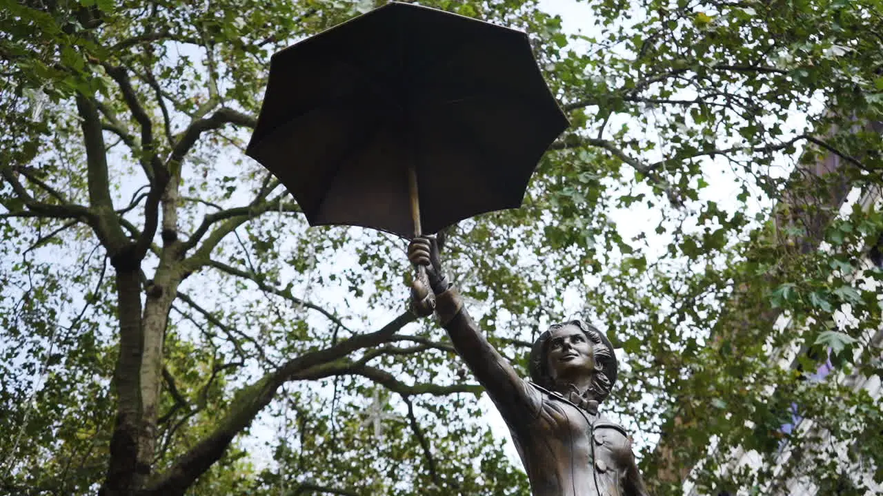 A Mary Poppins statue in Leicester Square London is surrounded by trees in the famous West End of the city