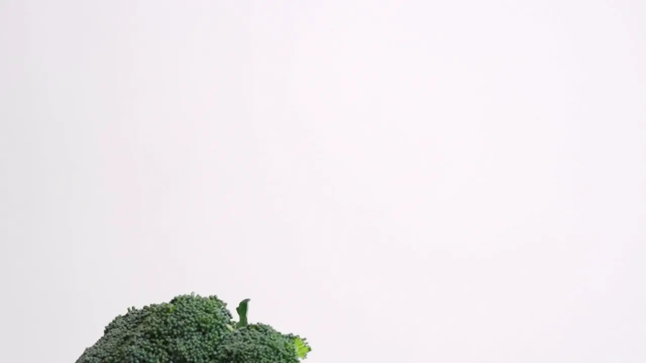 Whole head of broccoli falling in slow motion on white backdrop in 4k