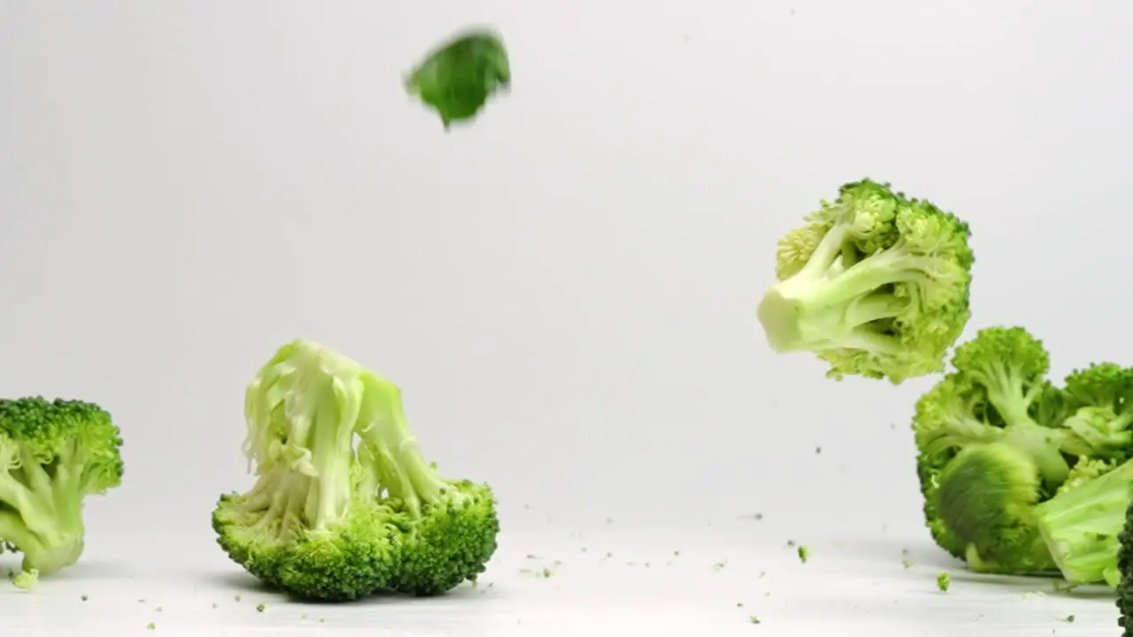 Broccoli pieces falling and bouncing in slow motion onto white studio backdrop in 4k