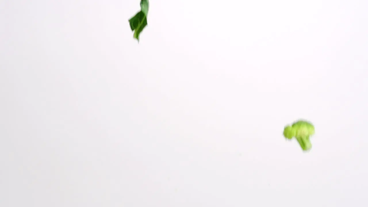 Broccoli pieces falling in slow motion on white studio backdrop in 4k slow motion