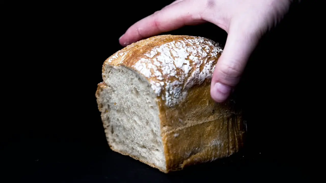 light bread is put down by hand in front of black background slow motion