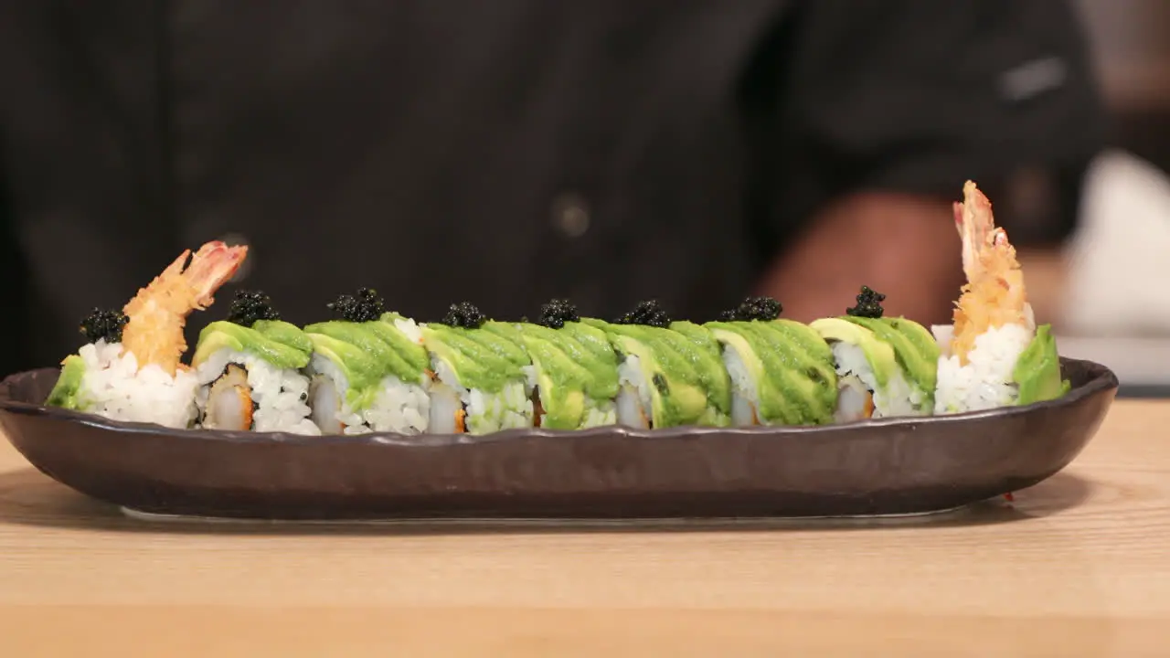 Chef Putting Roe On Top Of Shrimp Tempura Sushi Roll With Avocado Slices Using A Teaspoon close up panning shot