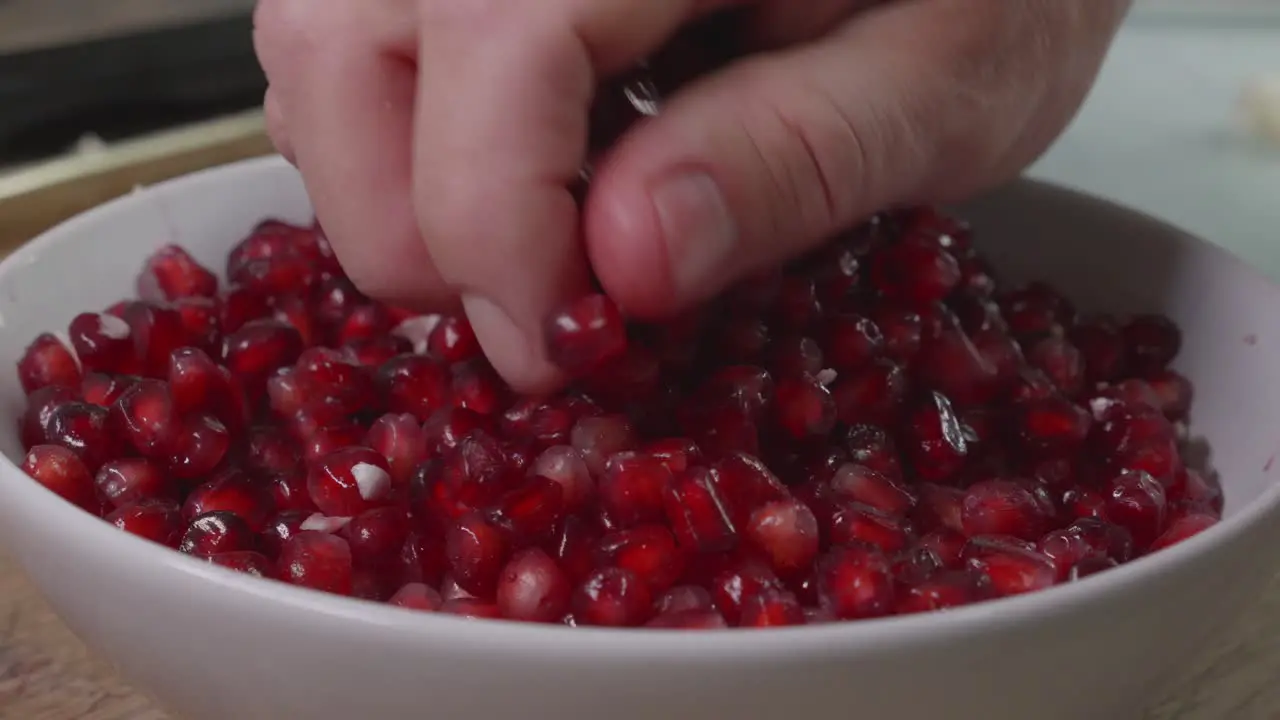 Medium close up of a mans hand in a bowl of pomegranate