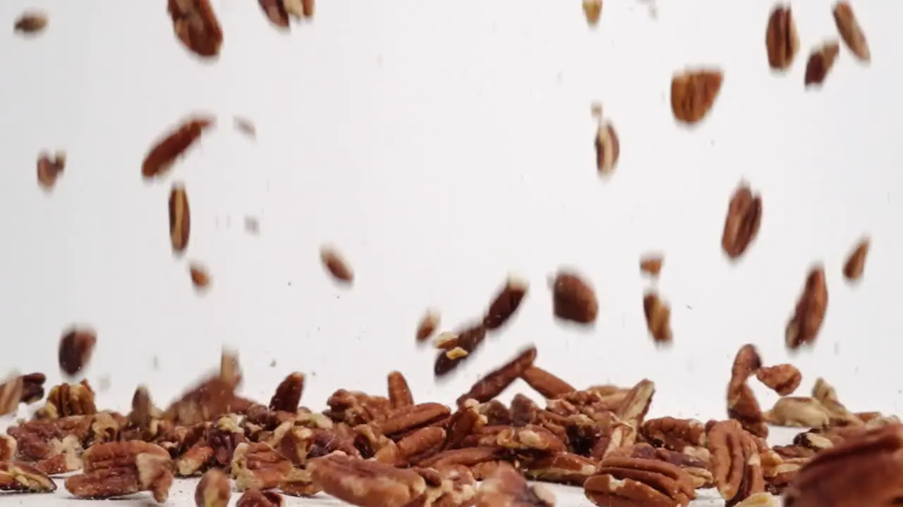 Pecan nut pieces raining down onto white table top and bouncing into a pile in slow motion