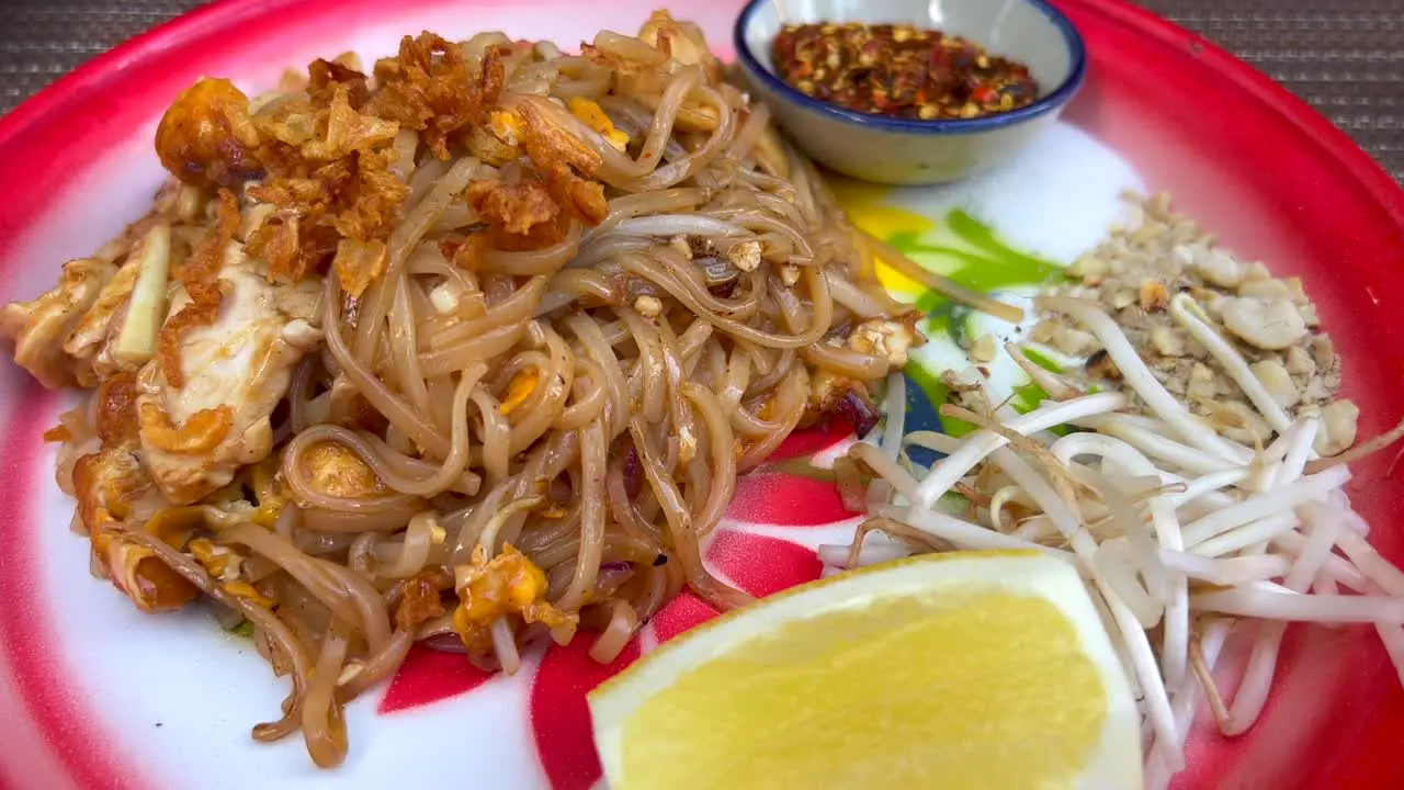 Spicy Pad Thai noodles dish with chicken crispy onion bean sprouts peanuts and chili flakes at a Thai restaurant tasty traditional asian food 4K shot