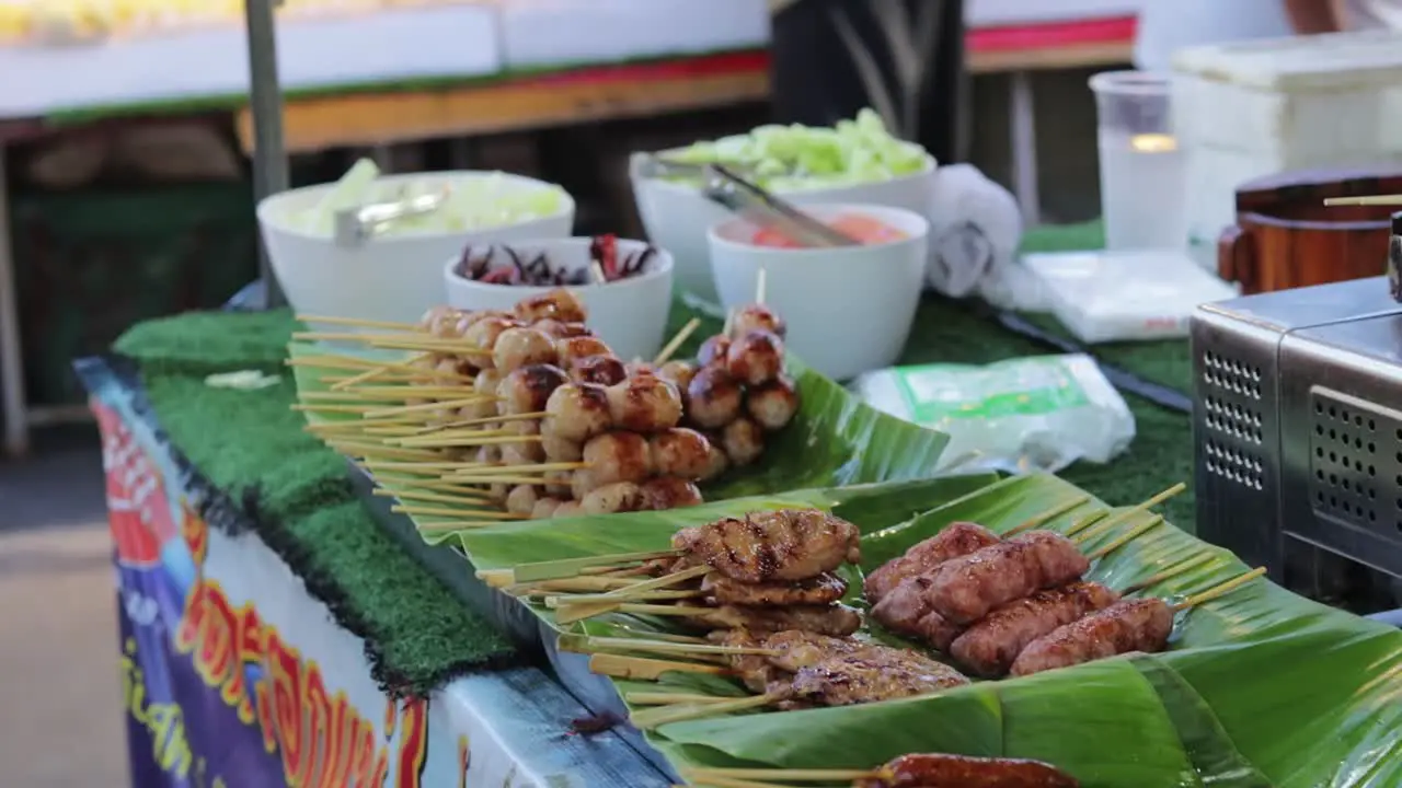 A close-up shot of pork meat meatballs skewers and other grilled meat in a local street market with customers walking