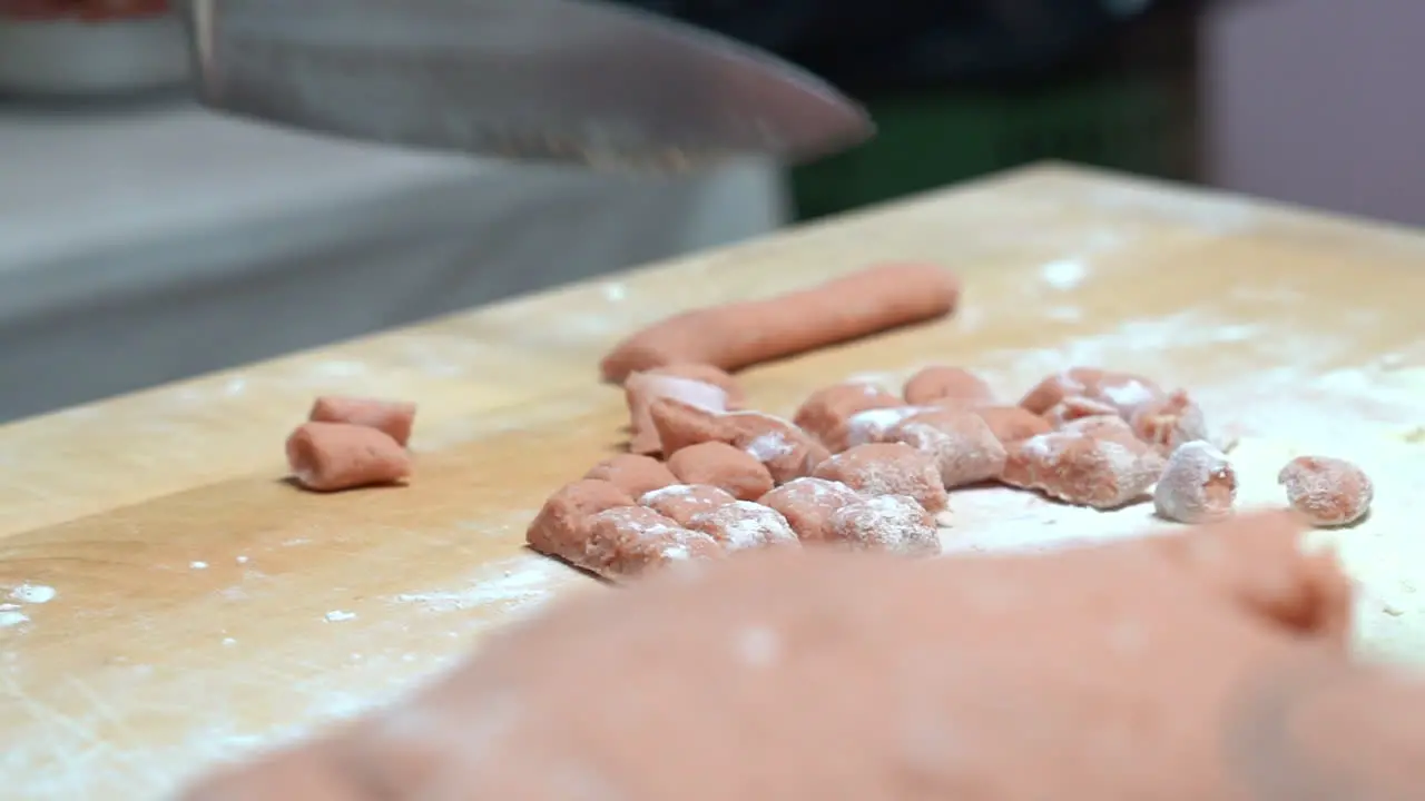 hands that grasp a knife that cuts small pieces of pasta on a wood table