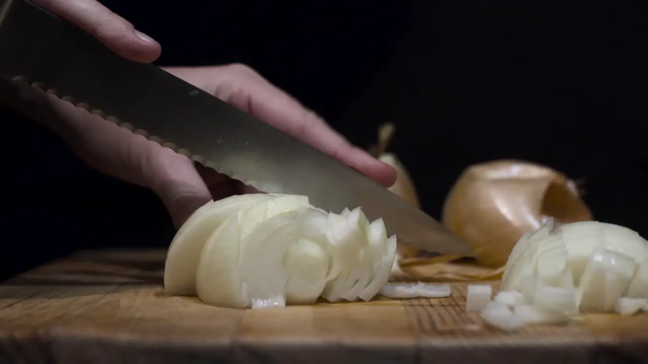 Close up shot of lady cutting onions on cutting board with black background