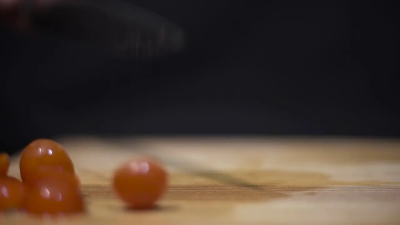 Close up shot of someone cutting cherry-grape tomatoes on cutting board with black background