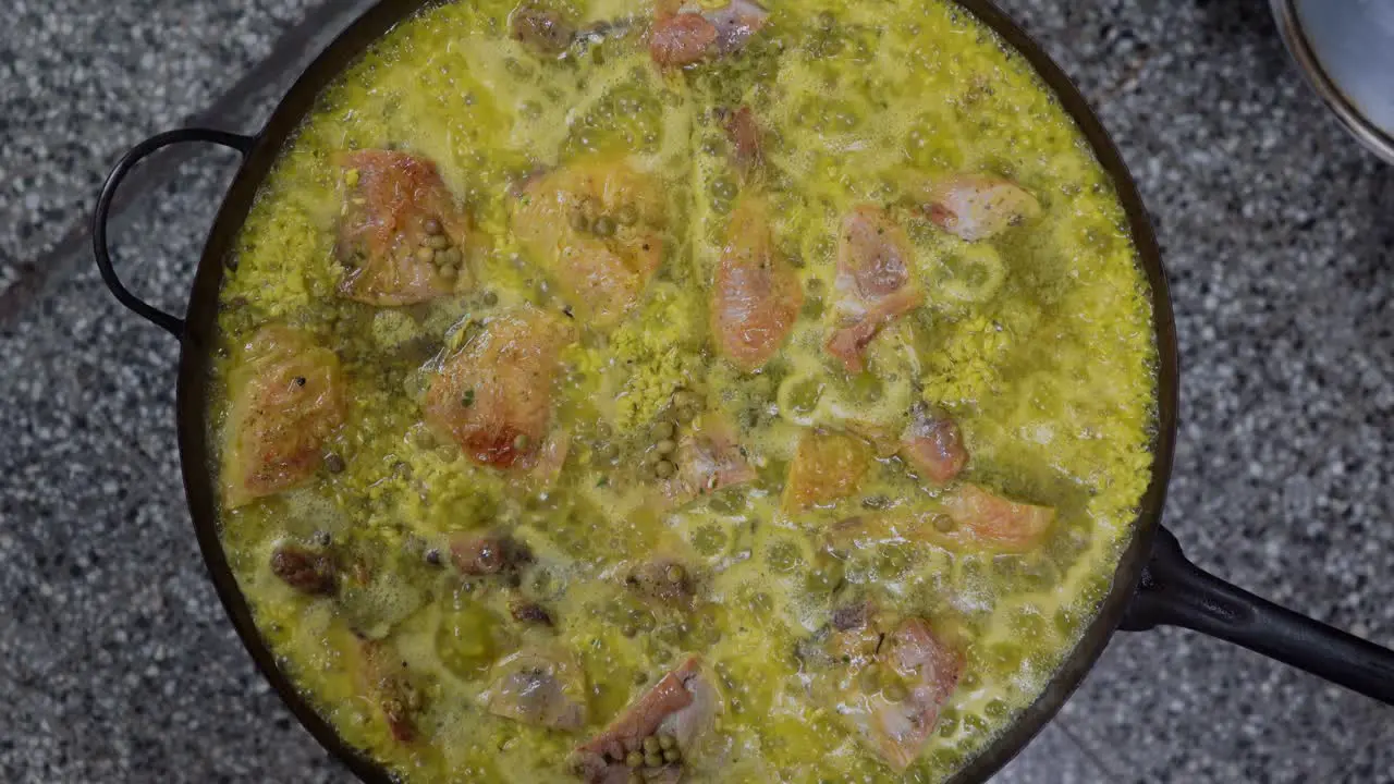 Top View Of Delicious Spanish Paella With Green Peas Chicken And Rice Simmering In A Large Pan In The Kitchen close up