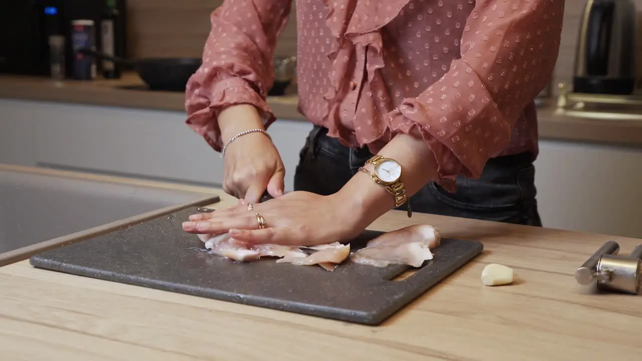 Elegantly dressed woman cutting chicken breast into slices on a cutting board in a kitchen