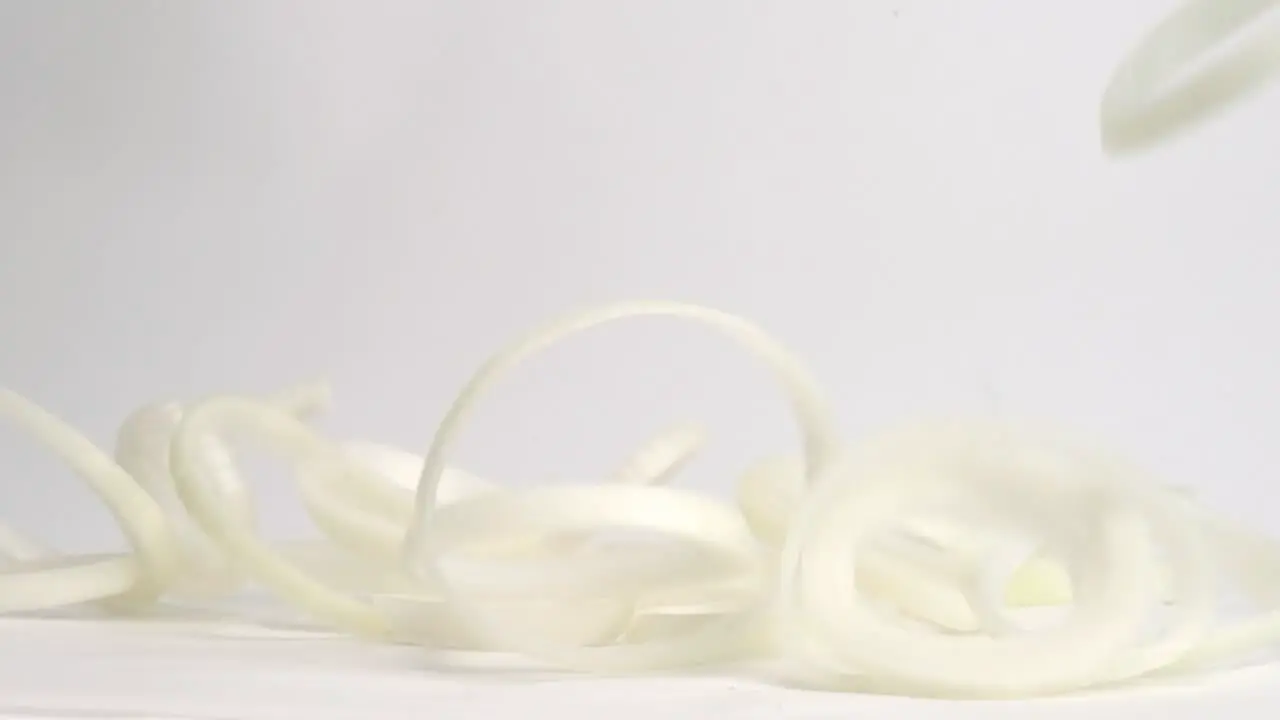 Perfectly round white onion ring circles falling and bouncing on white table top in slow motion