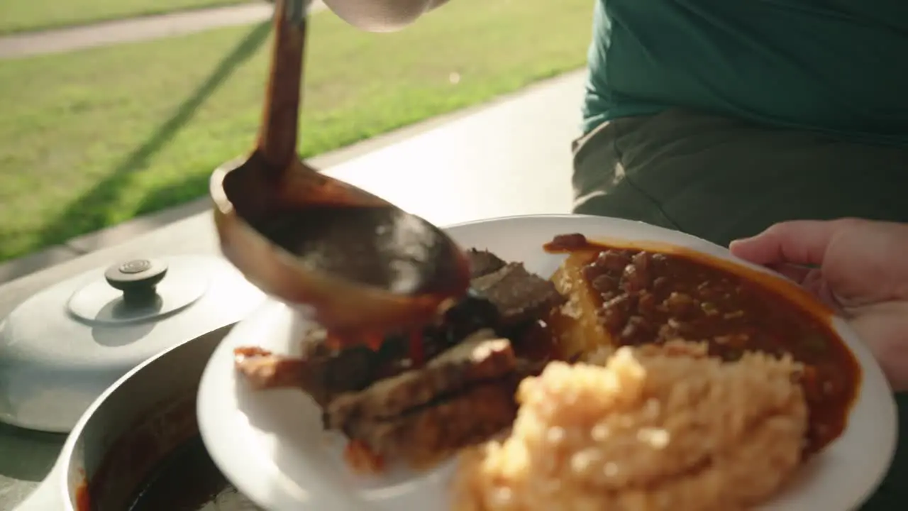 Chef ladles bbq sauce over plate full of food on paper plate to patron at soup kitchen buffet