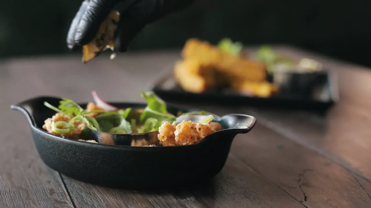 Chefs hand squeezing a lemon over a dish with sea food and herbs