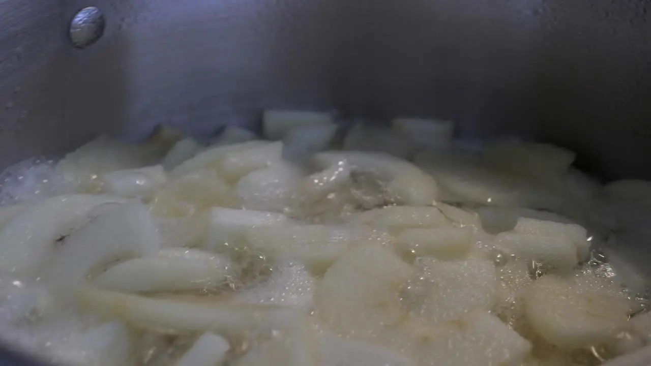 Slow pan around bubbling metal kitchen pot with lots of cut stewed apple in pieces boiling in water