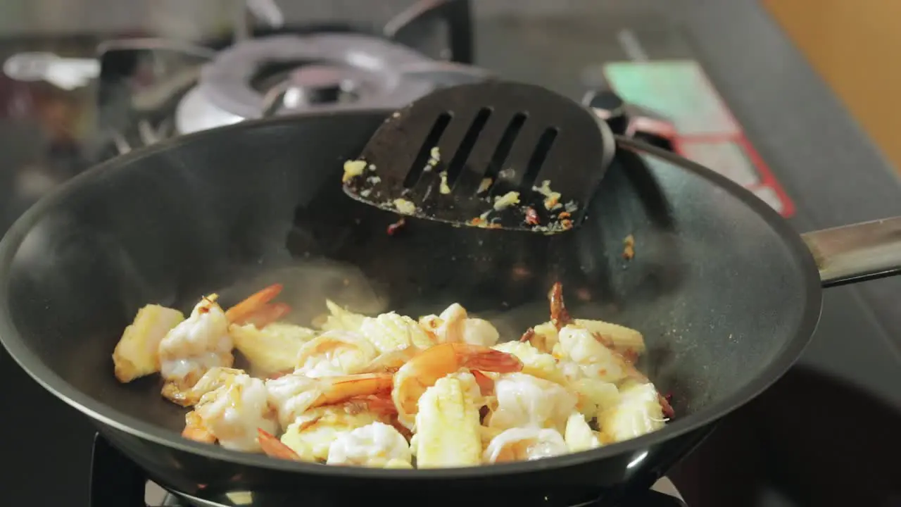 A woman is adding light soya sauce oyster sauce and sugar to frying shrimps preparing spicy fried shrimp with basil menu thai recipe