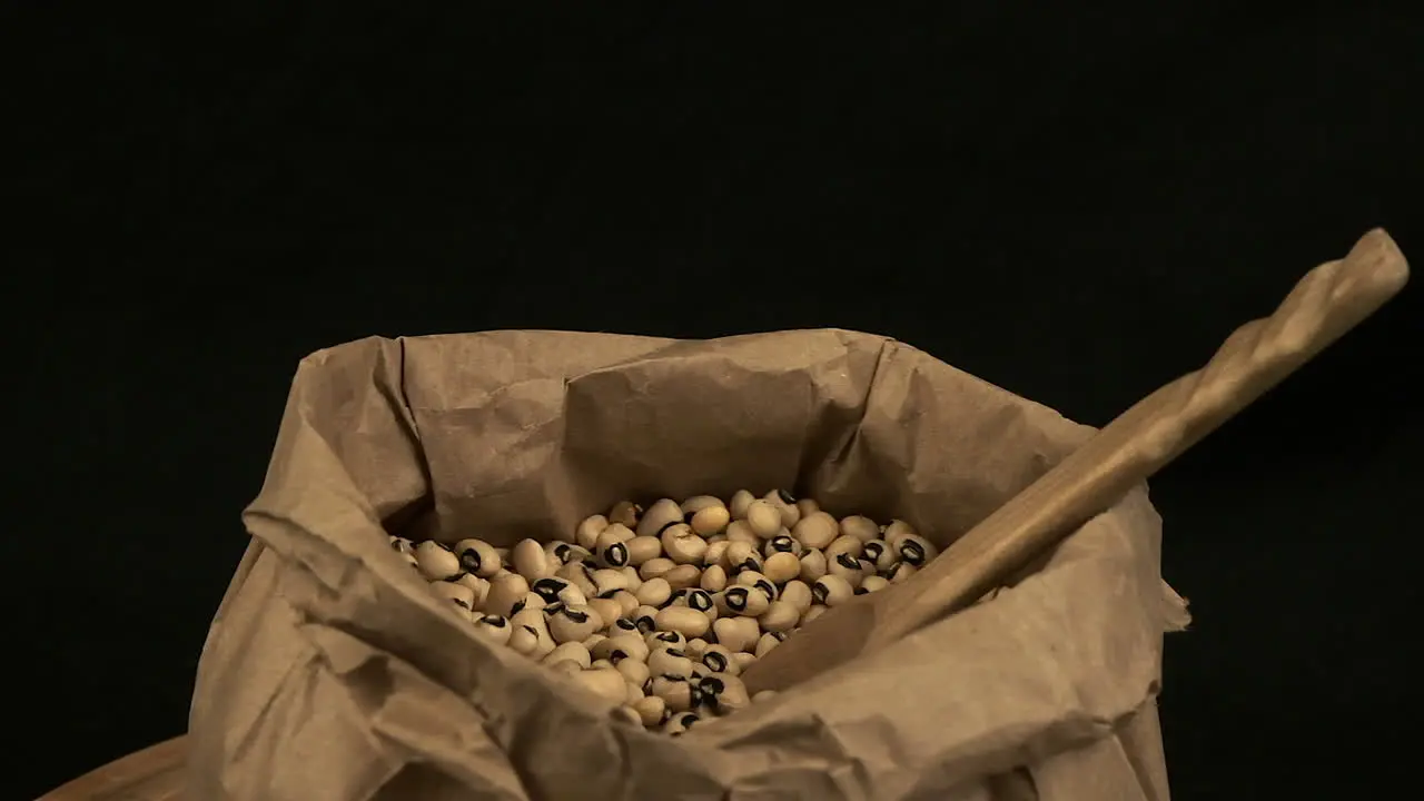 Wooden spoon in paper bag of dried black-eyed peas isolated on black