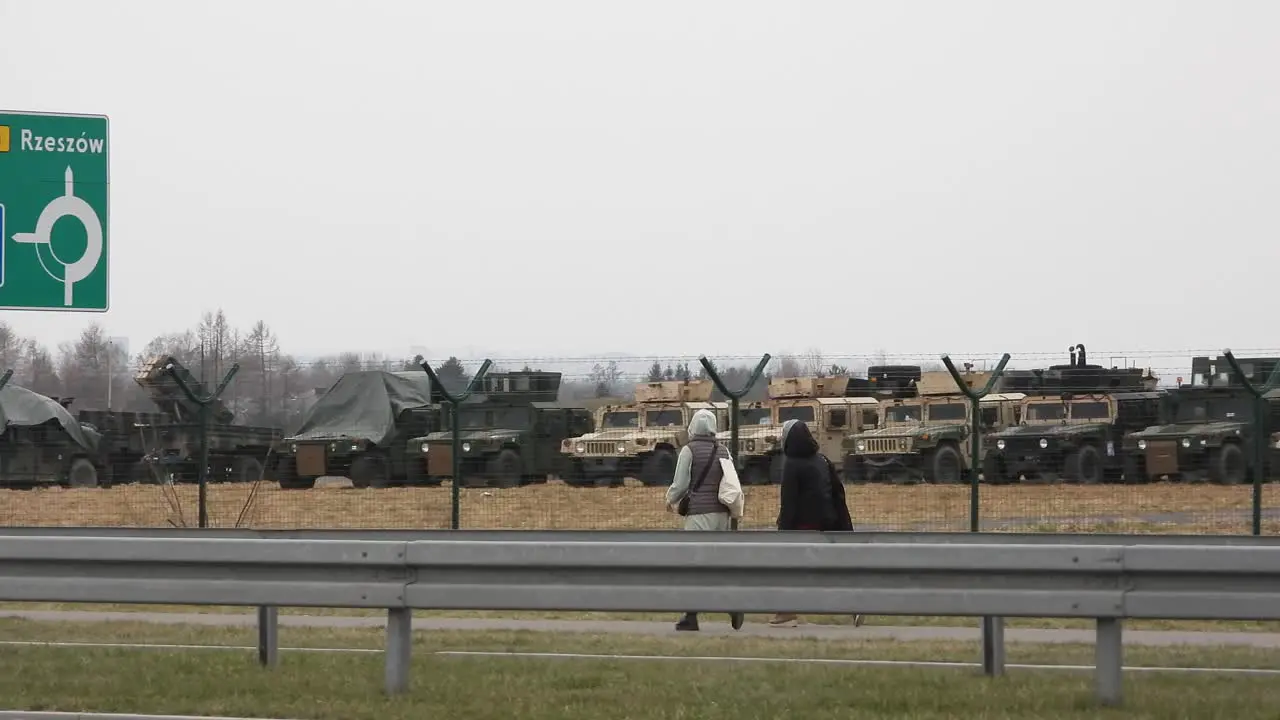 Two women pass military equipment destined for the Russia Ukraine conflict along a busy urban road