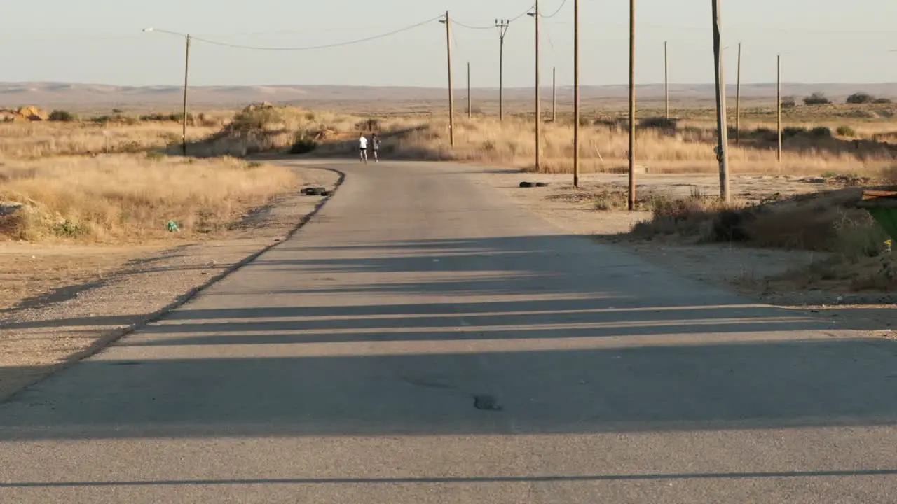 Static footage of a single road with old power poles in the middle of the desert near a military base as two soldiers run in the background