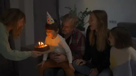 Little boy blows out the candles on dream the cake in a circle of happy family