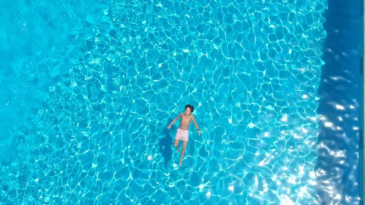 From a drone a child swims calmly over a pool of blue water