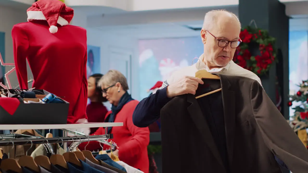 Senior man browsing blazers in festive clothing store during winter holiday season looking at formal attire pieces doing Christmas shopping spree in xmas decorated shop