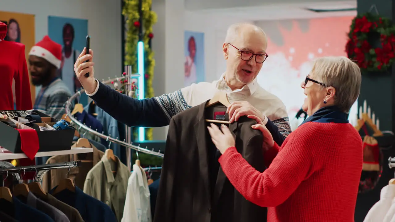 Cheerful elderly couple shopping for clothes while on online videocall with son helping them pick perfect Christmas gift before festive family dinner visit during winter holiday season