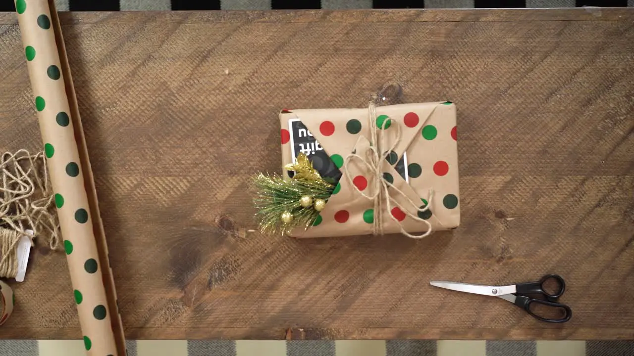 A young woman wraps a holiday Christmas present on a wooden table in polka dot wrapping paper a card and a mistletoe ready to put under the Xmas tree