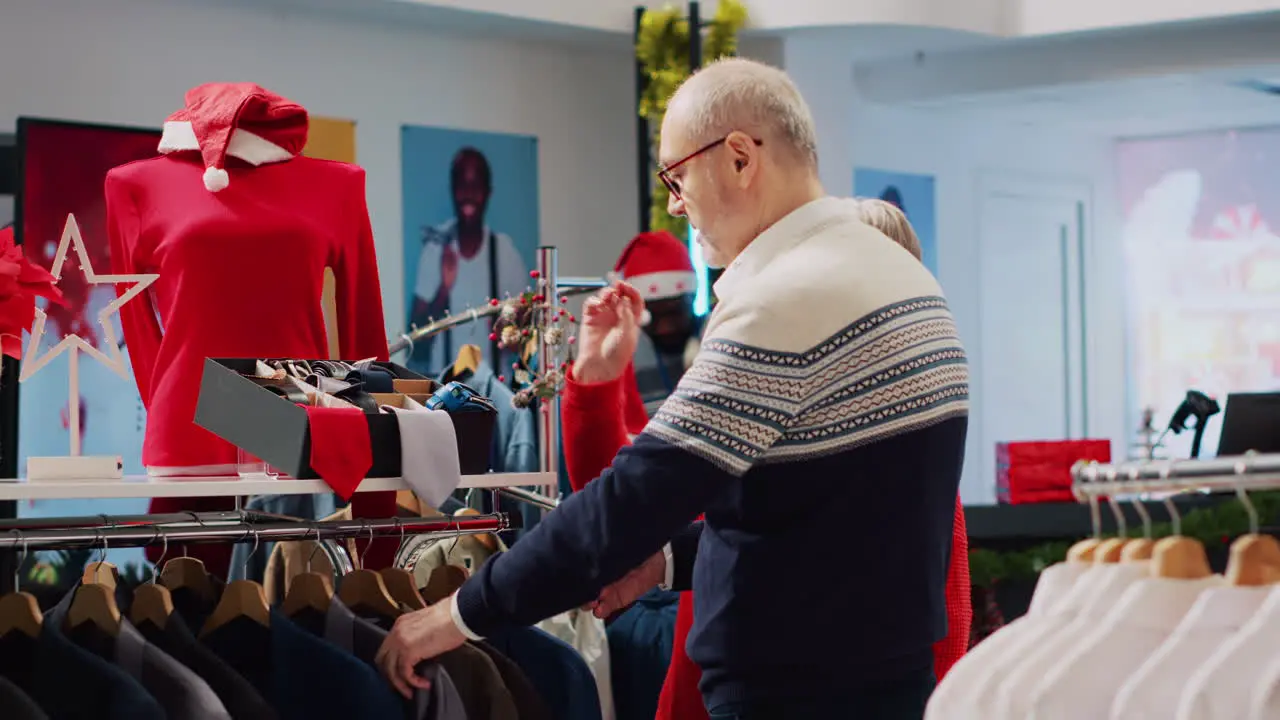 Senior customer browsing through xmas decorated clothing store racks with husband in Christmas shopping spree Aged couple searching for stylish blazer as present for son during winter holiday season