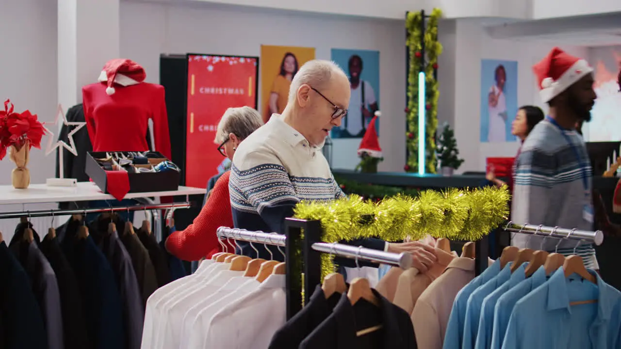 Senescent customers browsing through clothing racks in festive ornate fashion boutique during xmas holiday season Aged couple happy after finding colorful blazers to gift at Christmas family event