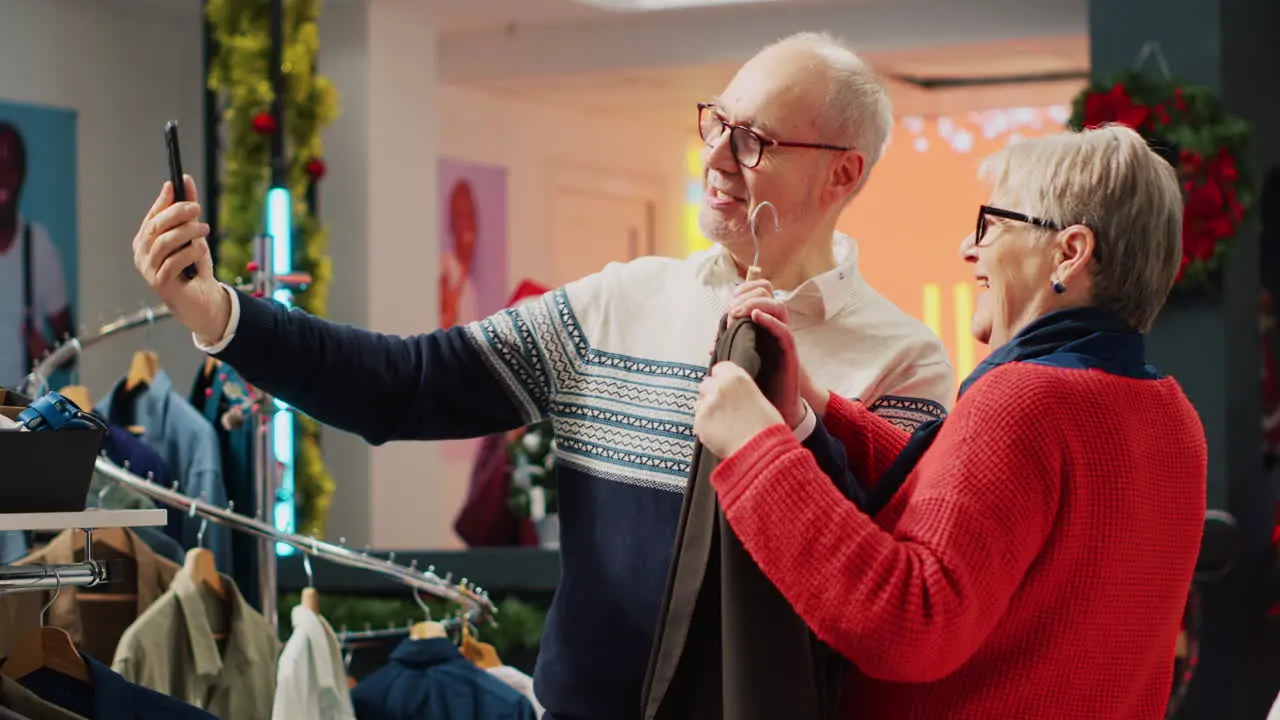 Happy senior couple shopping for clothes while on internet videocall with nephew asking for advice on picking perfect xmas present before festive family dinner visit during festive holiday season