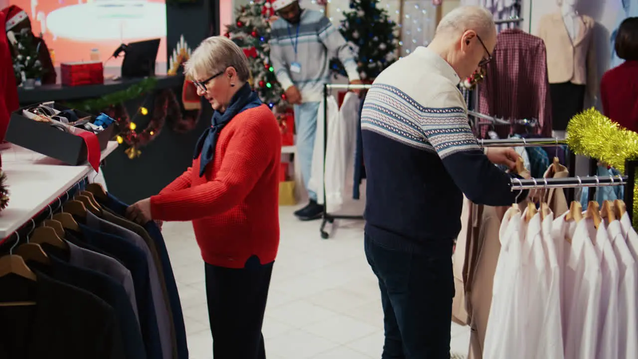 Older wife and husband browsing through clothing racks in Christmas decorated clothing store Elderly couple happy after finding perfect blazers to give as gift to grandson