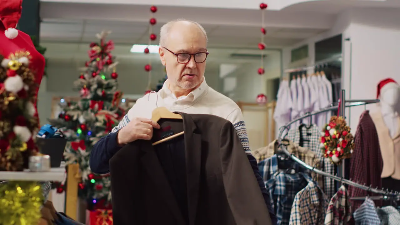 Older man examining elegant blazers in busy bustling shopping store during winter holiday season Elderly customer in Christmas decorated store checking clothing size looking for perfect fit