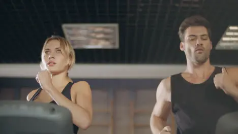 Concentrated couple running together on treadmill machine in gym club