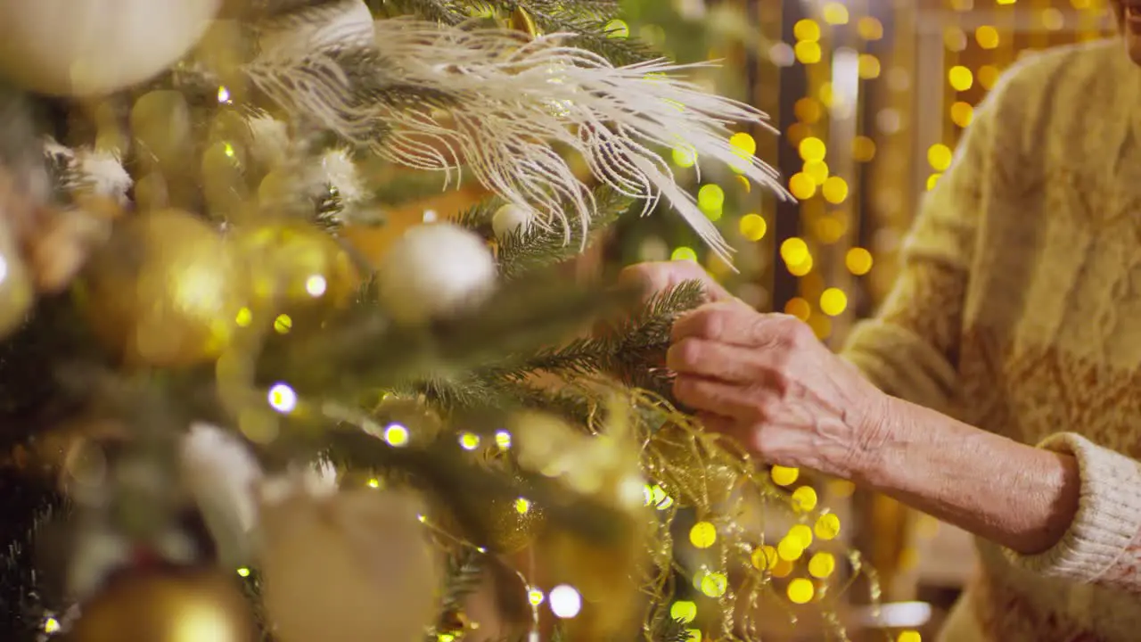 Older Woman Approaching The Christmas Tree Hangs Christmas Decorations