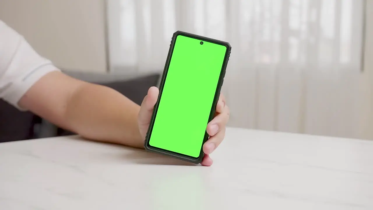 Man's hand shows mobile smartphone with green screen in vertical position isolated on green background