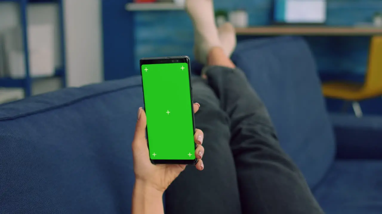 Freelancer woman lying on sofa looking at mock up green screen chroma key smartphone