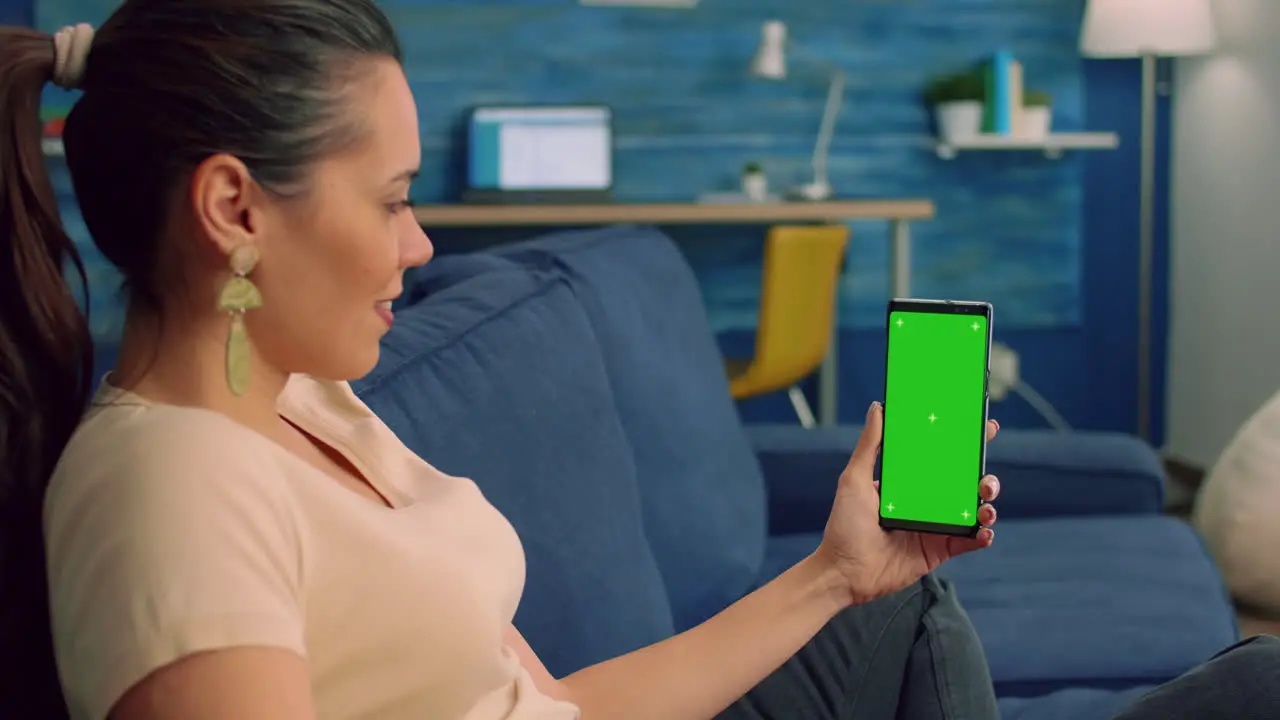 Freelancer woman sitting on sofa bed in living room looking at isolated smartphone