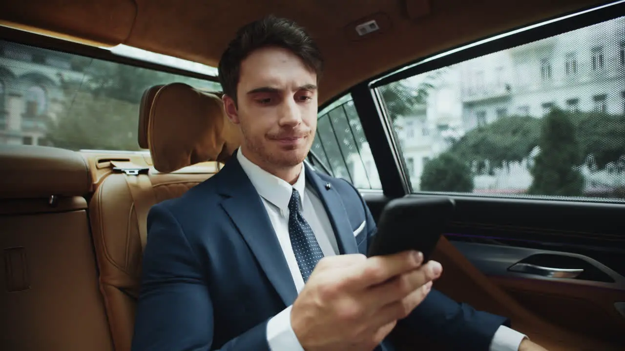 Upset male professional reading bad news on smartphone in salon of business car