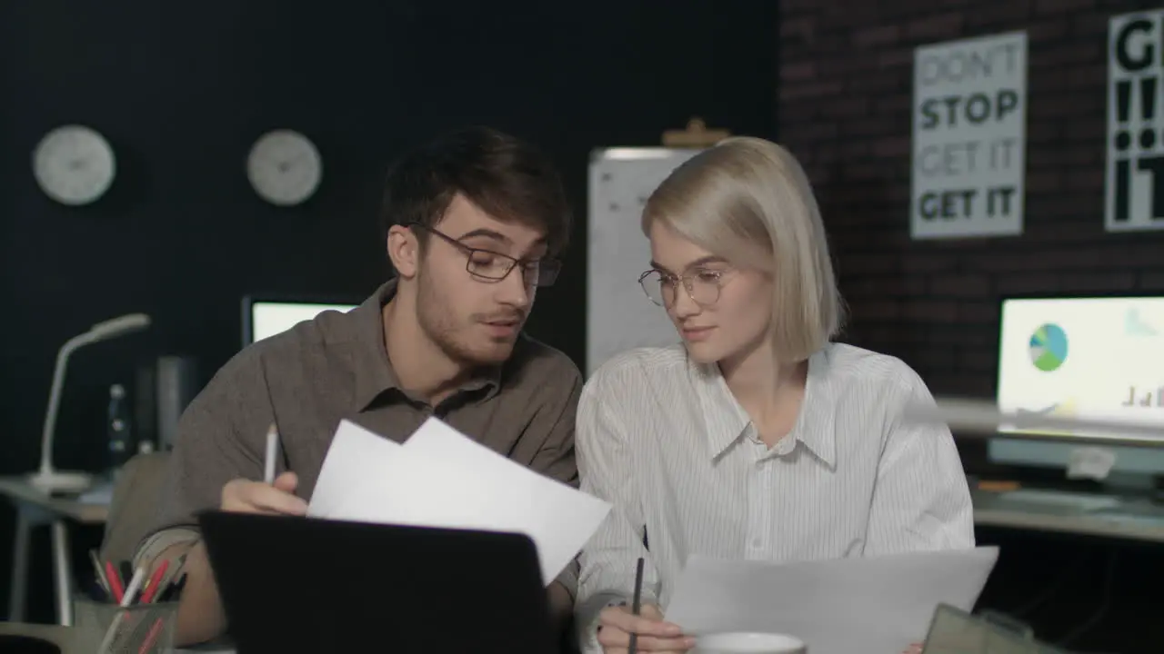 Young business man and woman working together front laptop in dark office